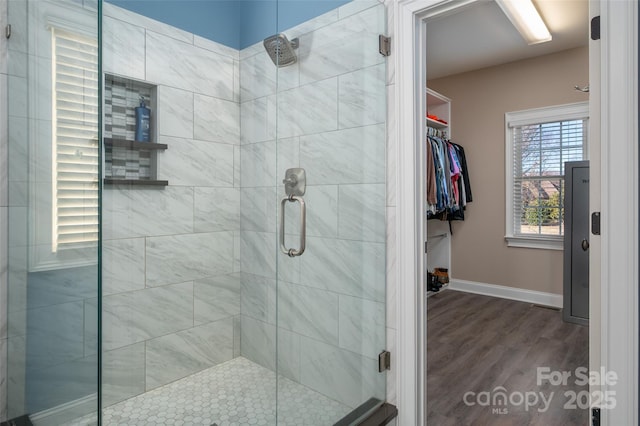 bathroom featuring baseboards, a spacious closet, wood finished floors, and a shower stall