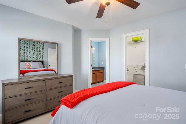 bedroom with connected bathroom, light carpet, a spacious closet, and a ceiling fan