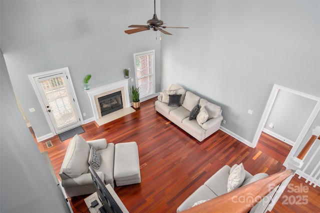 living area with a fireplace with flush hearth, wood finished floors, and a towering ceiling