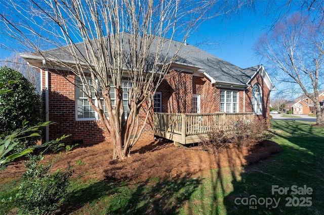 view of property exterior with brick siding, a deck, and a yard