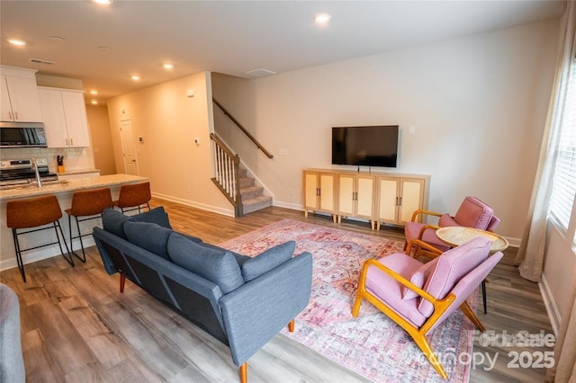 living area with baseboards, stairway, light wood-style flooring, and recessed lighting