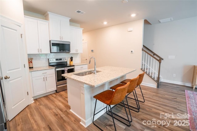 kitchen with visible vents, an island with sink, stainless steel appliances, white cabinetry, and a sink