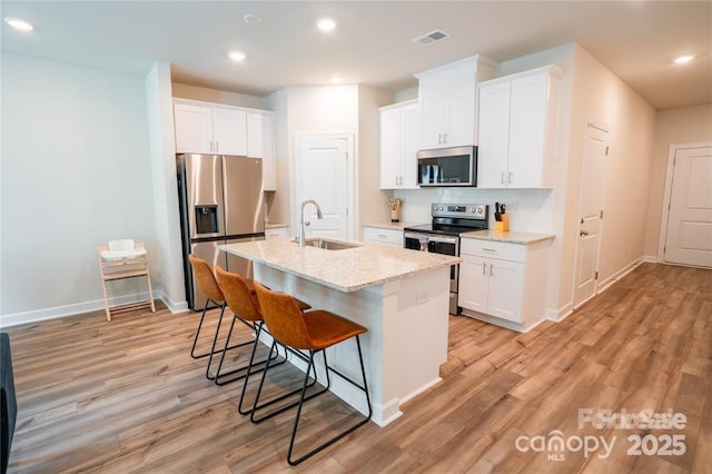 kitchen featuring appliances with stainless steel finishes, a sink, white cabinets, and a kitchen breakfast bar