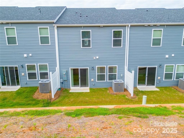 back of property with a yard, central AC unit, and a shingled roof