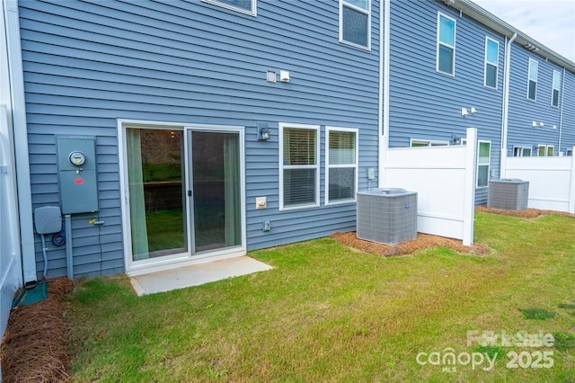 rear view of house with central air condition unit, fence, and a lawn