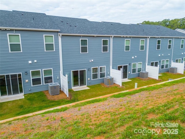 rear view of property with central AC unit, a lawn, and roof with shingles