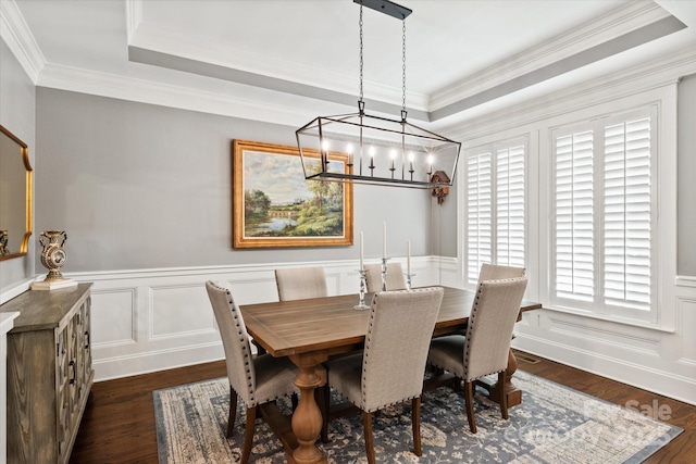 dining room featuring a decorative wall, a wainscoted wall, dark wood-type flooring, a tray ceiling, and crown molding