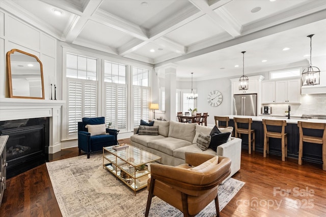 living room with coffered ceiling, a fireplace with flush hearth, dark wood-style flooring, an inviting chandelier, and beam ceiling