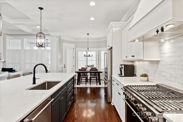 kitchen with premium appliances, a notable chandelier, custom range hood, white cabinetry, and a sink