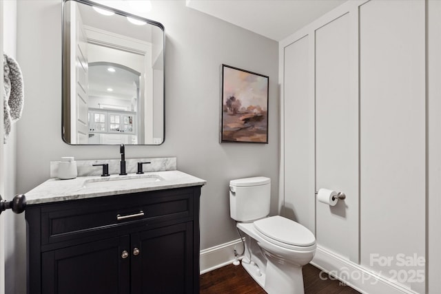half bath featuring toilet, baseboards, wood finished floors, and vanity