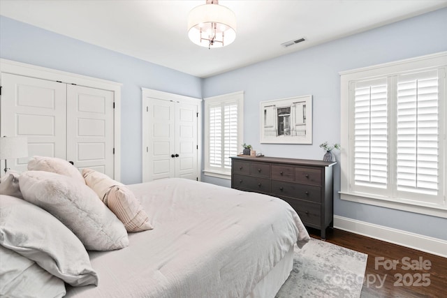 bedroom featuring visible vents, baseboards, dark wood finished floors, and multiple closets