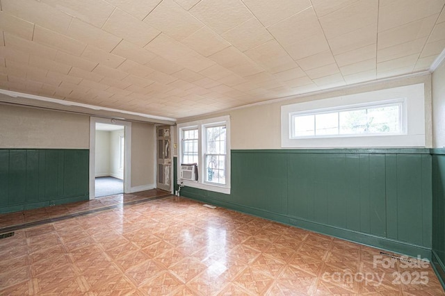 unfurnished room featuring crown molding, a wainscoted wall, plenty of natural light, and visible vents