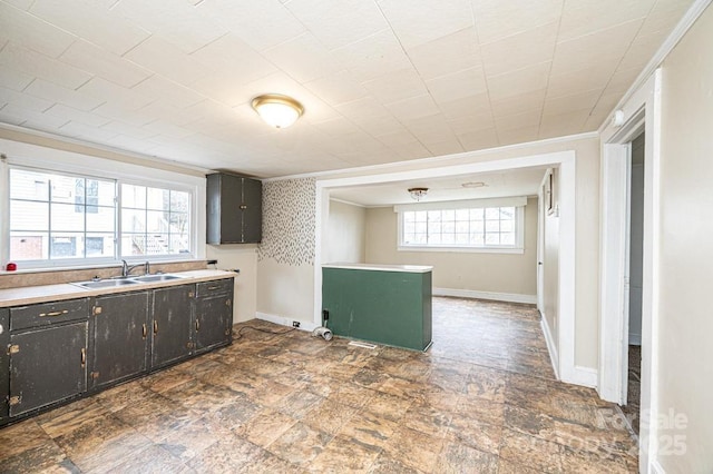 kitchen with stone finish flooring, ornamental molding, a sink, and baseboards