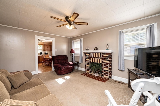 carpeted living area with a brick fireplace, baseboards, a ceiling fan, and crown molding