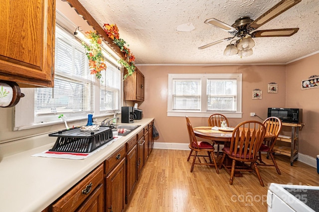 kitchen with brown cabinets, crown molding, light countertops, light wood-style floors, and a sink