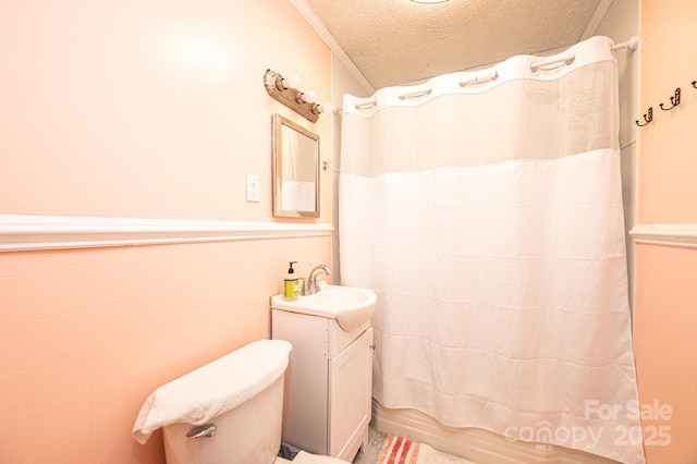 bathroom featuring a wainscoted wall, shower / bathtub combination with curtain, toilet, a textured ceiling, and vanity