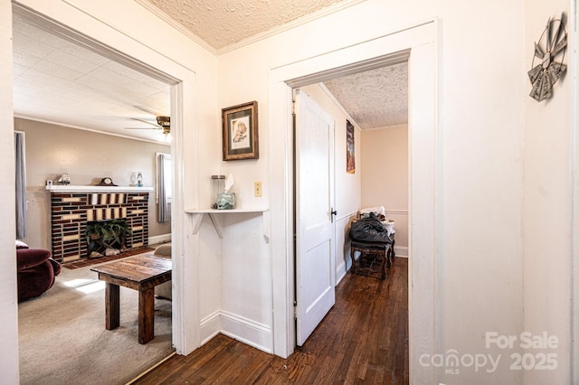 corridor featuring dark wood-style floors, baseboards, ornamental molding, and a textured ceiling