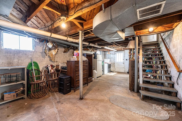 below grade area featuring freestanding refrigerator, stairway, washer / dryer, and visible vents