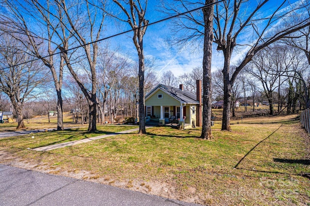 view of front of home with covered porch, a chimney, and a front lawn