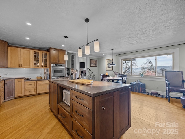 kitchen featuring oven, light wood-style flooring, dark countertops, a center island, and glass insert cabinets