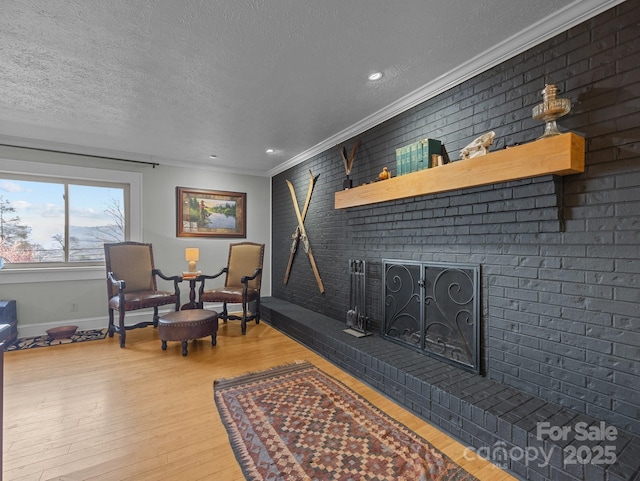 sitting room featuring wood finished floors, brick wall, a fireplace, a textured ceiling, and crown molding