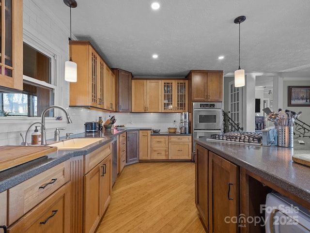 kitchen with a sink, stainless steel appliances, light wood-type flooring, and dark countertops