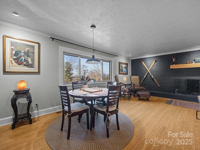 dining space with light wood finished floors, a textured ceiling, baseboards, and ornamental molding