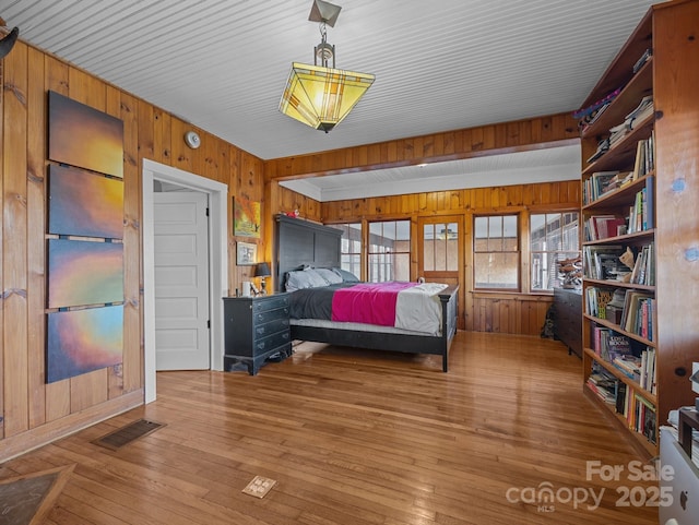 bedroom featuring hardwood / wood-style flooring, visible vents, and wood walls