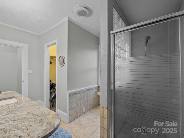 full bathroom featuring tile patterned flooring, a shower stall, crown molding, a walk in closet, and a sink