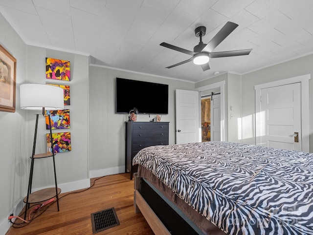 bedroom featuring visible vents, wood finished floors, a barn door, baseboards, and ceiling fan