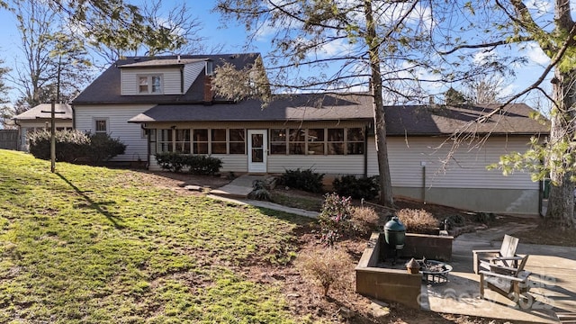 rear view of house featuring a shingled roof, an outdoor fire pit, a yard, a sunroom, and a patio area