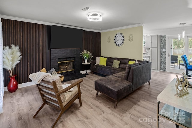 living room featuring ornamental molding, light wood-type flooring, a brick fireplace, and visible vents