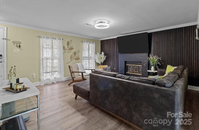 living room featuring a fireplace, wood finished floors, visible vents, baseboards, and ornamental molding