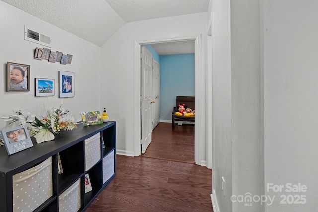 hallway with a textured ceiling, visible vents, baseboards, vaulted ceiling, and dark wood finished floors