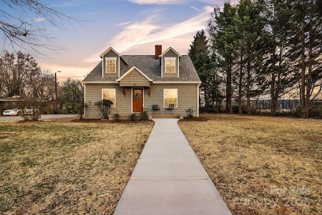 view of front of home featuring a shingled roof, a chimney, and a lawn