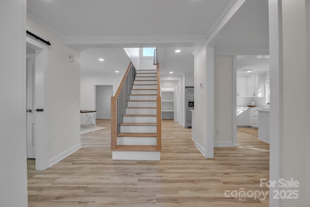 staircase with a barn door, recessed lighting, wood finished floors, baseboards, and crown molding