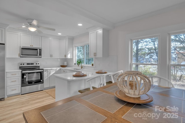 kitchen with decorative backsplash, white cabinets, appliances with stainless steel finishes, a peninsula, and light countertops