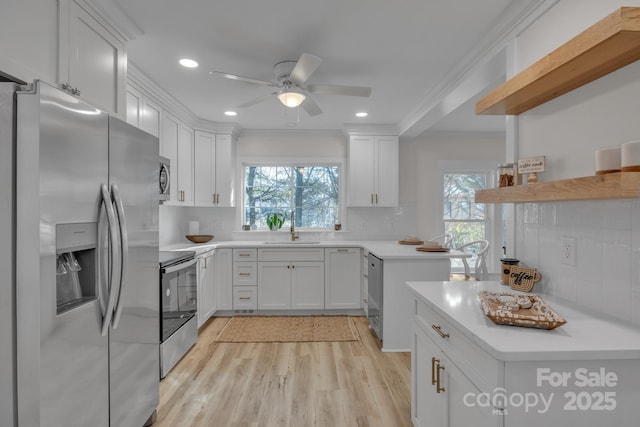 kitchen with stainless steel appliances, light countertops, ornamental molding, white cabinetry, and a sink