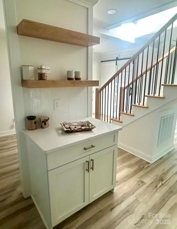 bar with light wood finished floors, stairway, visible vents, and baseboards