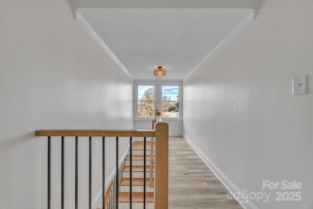 corridor with a textured ceiling, an upstairs landing, baseboards, light wood finished floors, and crown molding