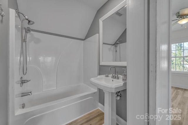 bathroom featuring shower / bathtub combination, a sink, wood finished floors, baseboards, and vaulted ceiling