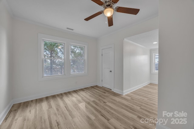 spare room featuring visible vents, ornamental molding, a ceiling fan, wood finished floors, and baseboards