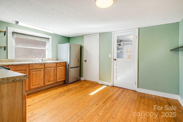 kitchen with light wood-style flooring, freestanding refrigerator, a sink, a textured ceiling, and baseboards