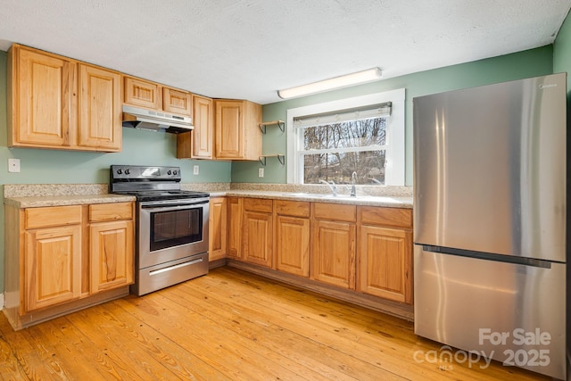 kitchen with light countertops, appliances with stainless steel finishes, a sink, light wood-type flooring, and under cabinet range hood