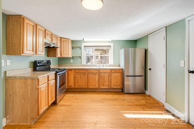 kitchen featuring a textured ceiling, under cabinet range hood, stainless steel appliances, light countertops, and light wood-type flooring