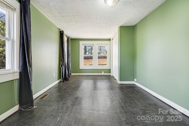 empty room featuring baseboards, visible vents, and a textured ceiling