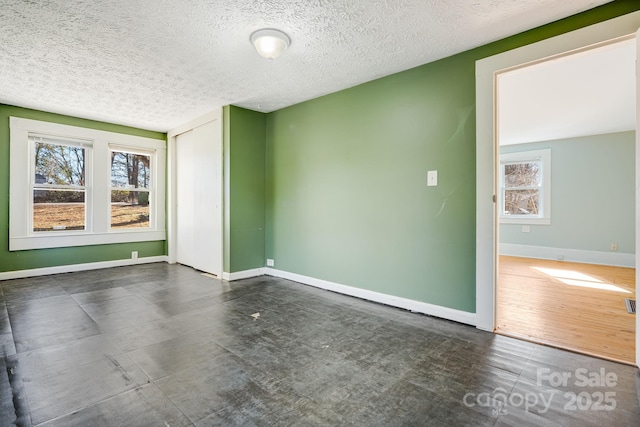 empty room featuring a healthy amount of sunlight, a textured ceiling, and baseboards