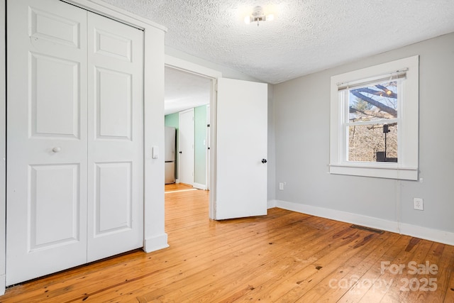 unfurnished bedroom with a textured ceiling, visible vents, baseboards, light wood-style floors, and freestanding refrigerator