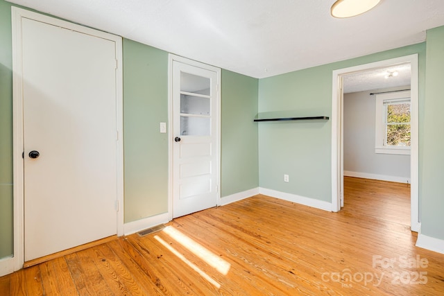 unfurnished bedroom featuring light wood-style flooring, visible vents, baseboards, and a closet