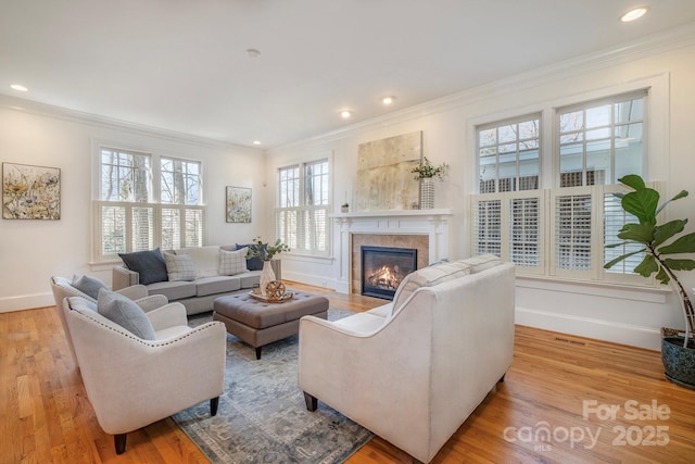 living room featuring light wood-type flooring, a glass covered fireplace, crown molding, and baseboards